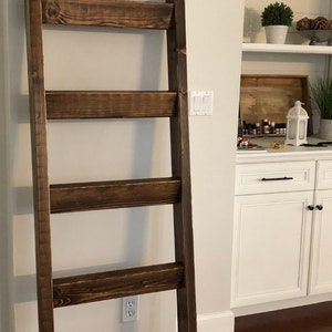 May include: A dark brown wooden ladder shelf with five shelves. The ladder shelf is standing on a wooden floor.