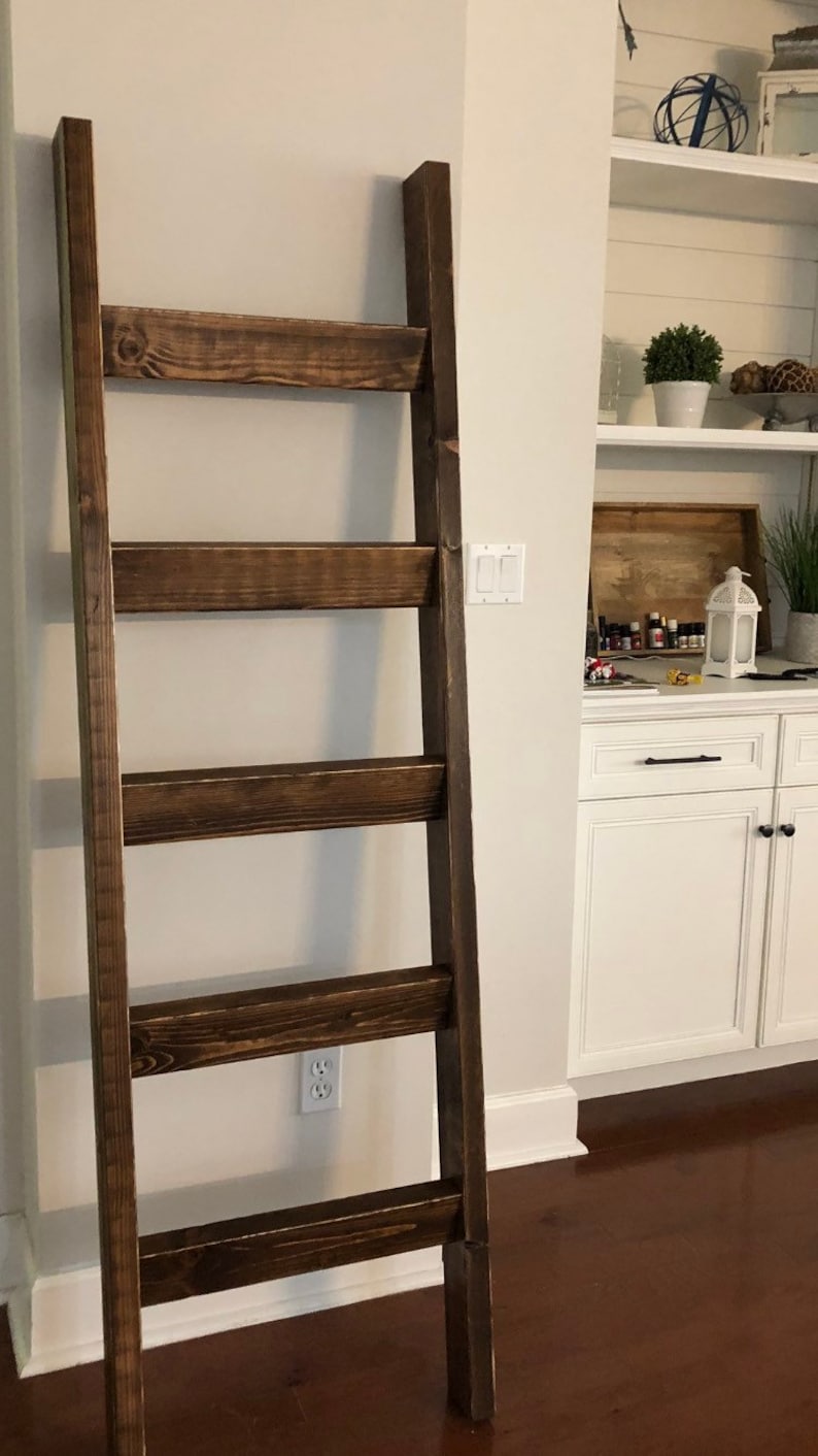 May include: A dark brown wooden ladder shelf with five shelves. The ladder shelf is standing on a wooden floor.