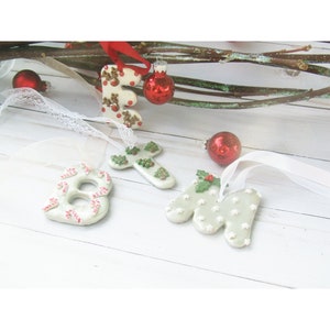 May include: Christmas-themed ornaments in the shape of the letter "E", the number "8", a cross, and the letter "M". The ornaments are white with festive decorations, including reindeer, candy canes, Christmas trees, and stars. Red ornaments and ribbon complete the holiday scene.