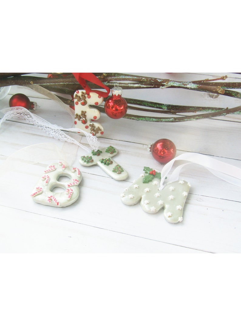 May include: Christmas-themed ornaments in the shape of the letter "E", the number "8", a cross, and the letter "M". The ornaments are white with festive decorations, including reindeer, candy canes, Christmas trees, and stars. Red ornaments and ribbon complete the holiday scene.