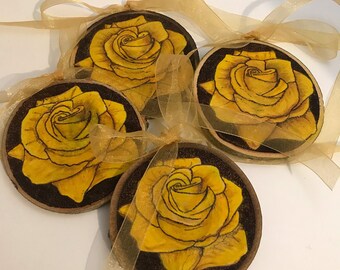 May include: Four round wood slices with painted yellow roses. The wood slices are painted with a dark brown background and have a natural wood edge.
