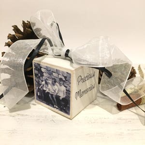 May include: A white wooden block with a black and white photo of people, tied with a sheer white ribbon and black ribbon. The block has the words "Precious Memories" written on it.