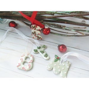 May include: Christmas-themed ornaments in the shape of letters and numbers, including the letters "E" and "N", and the number "8". The ornaments are white with red and green accents, and are decorated with reindeer, candy canes, and stars.