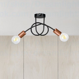 May include: A black ceiling light fixture with three copper-coloured arms and clear light bulbs. The fixture is mounted on a white ceiling.