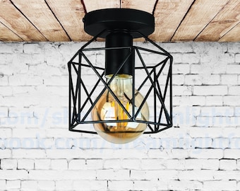 May include: Black caged ceiling light fixture with a geometric design. The light is on and a warm white light bulb is visible.