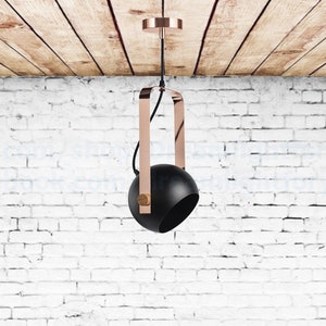 May include: A black pendant light with a copper finish hanging from a wooden ceiling. The light has a round black shade and a copper frame.