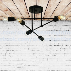 May include: Black ceiling light fixture with five arms and five light bulbs. The fixture is mounted on a white brick wall.