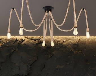 May include: A ceiling light fixture featuring six hanging light bulbs suspended by thick, beige twisted hemp ropes. The ropes are attached to a central black circular mount and extend outward to individual black ceiling hooks, creating a spider-like design.