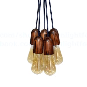 Puede incluir: Un grupo de seis lámparas colgantes con cubiertas de bombillas de madera oscura y cables negros que cuelgan de un techo.