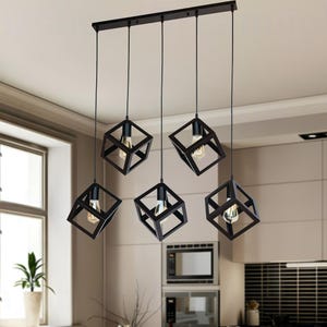 May include: A modern kitchen with a wooden dining table and six black cube pendant lights. The lights hang above the table, which is set with glasses and tableware. The kitchen has white cabinets and a black tile backsplash.