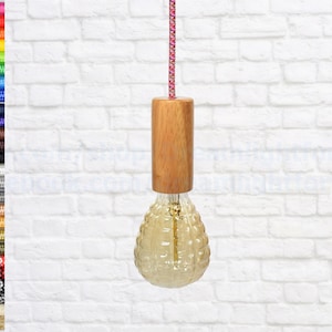 May include: A wooden pendant light fitting with a clear glass bulb. The bulb has a textured, honeycomb-like design. The fitting is hanging from a white brick wall.
