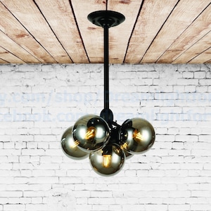 May include: A black metal chandelier with five round, smoked glass globes. The chandelier is hanging from a wooden ceiling.