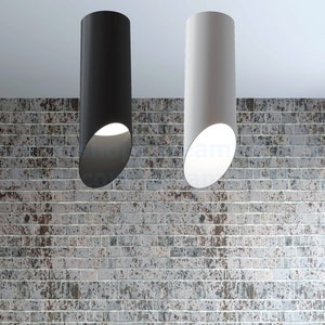 Puede incluir: Dos lámparas colgantes cilíndricas, una negra y otra blanca, colgando de un techo contra una pared de ladrillo.