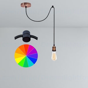 Może przedstawiać: Czarne wiszące oświetlenie z miedzianym gniazdkiem i przezroczystą szklaną żarówką wiszącą na czarnym przewodzie. Światło jest zawieszone na miedzianym mocowaniu sufitowym. Na tle widoczne jest koło kolorów tęczy.