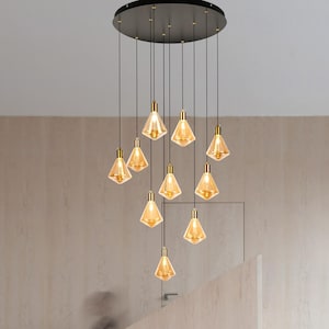 May include: A modern chandelier with ten amber-colored, geometric glass shades suspended from a black circular ceiling plate. Each shade has a gold-colored metal accent. The light fixture hangs in a neutral-toned room with a staircase.