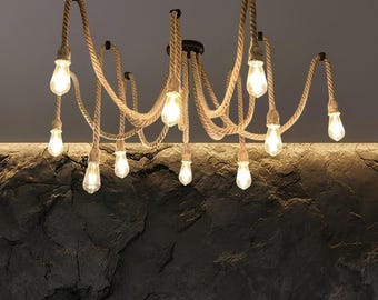 May include: A multi-arm chandelier featuring thick, tan-colored rope cords suspended from a central black ceiling mount. Each rope cord terminates in a clear glass light bulb, creating a sprawling, web-like arrangement of ten illuminated light sources.