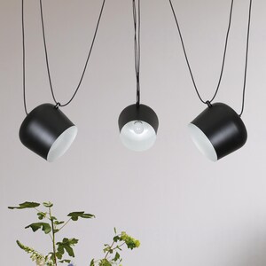 May include: Three black pendant lights with white interior shades hang from the ceiling. The lights are suspended by black cords.