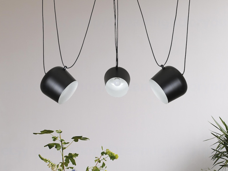 May include: Three black pendant lights with white interior shades hang from the ceiling. The lights are suspended by black cords.