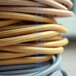 May include: Close-up of three spools of fabric cord in different colors: a light brown, a gold, and a silver. The cords are wound tightly together.