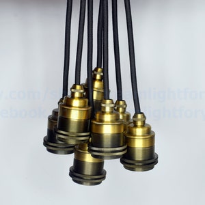 May include: A group of eight gold-toned metal lamp sockets with black electrical cords hanging from the ceiling.