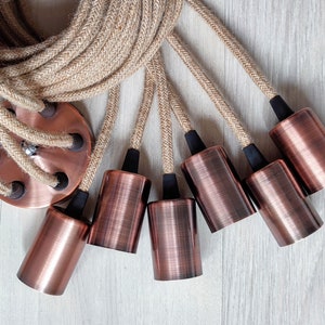 May include: A set of six copper-colored pendant light fixtures with black cords and a jute rope cord. The cords are wrapped around a copper-colored ceiling plate.