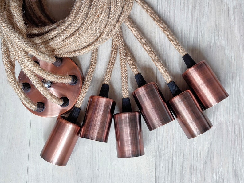 May include: A set of six copper-colored pendant light fixtures with black cords and a jute rope cord. The cords are wrapped around a copper-colored ceiling plate.