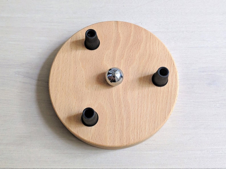 May include: A round wooden ceiling plate with three black electrical cord holders and a silver metal ball in the center.