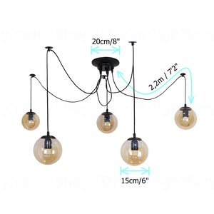 May include: Black pendant light fixture with five amber glass globe shades. The fixture has adjustable cords, with a maximum length of 72 inches and a width of 20 inches. The globes are 6 inches in diameter.
