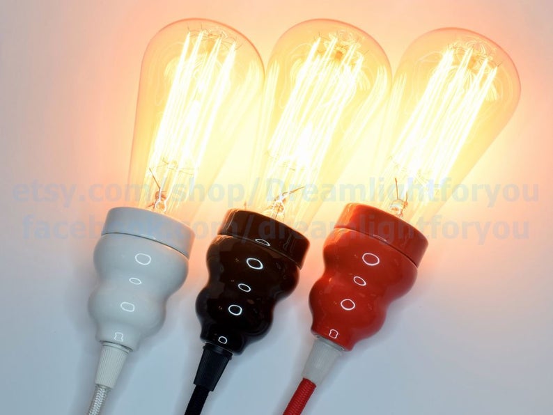 May include: Three vintage-style light bulbs with exposed filaments, each with a different colored ceramic socket: white, black, and red. The bulbs are lit and glowing.