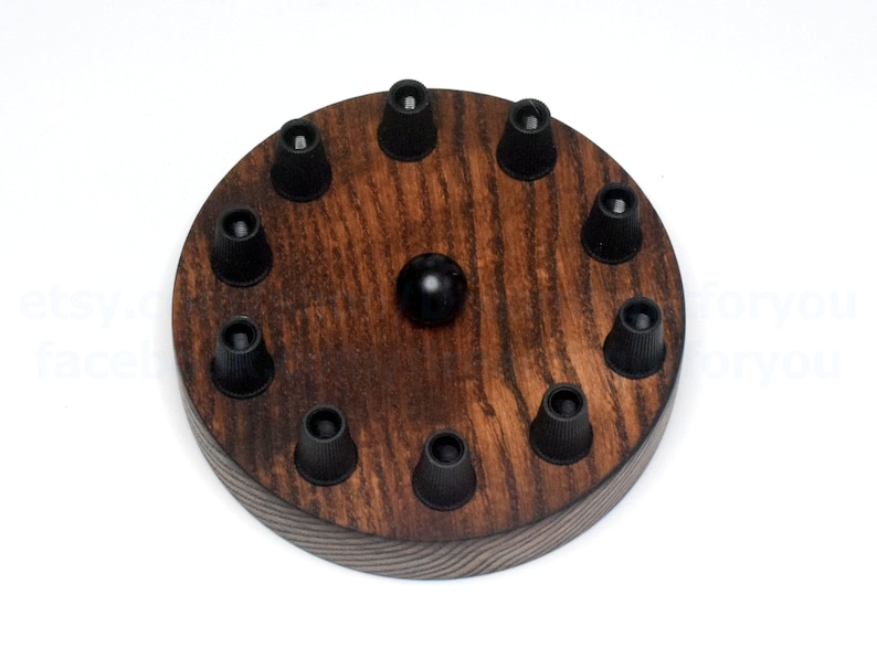 K&ouml;nnte beinhalten: Eine runde Holz-Deckenrosette mit acht schwarzen Kabelhaltern und einem schwarzen Mittelknopf. Das Holz ist dunkelbraun mit einer Holzmaserung.