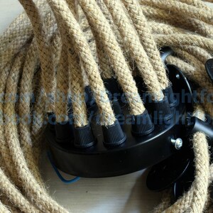 May include: Close-up of a multi-strand, natural rope cord with black electrical connectors. The rope is woven and has a natural, rustic look.