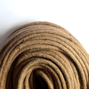 May include: A close-up of a tightly wound coil of natural brown jute rope. The rope is made of thick, twisted fibers and has a rough, textured surface.