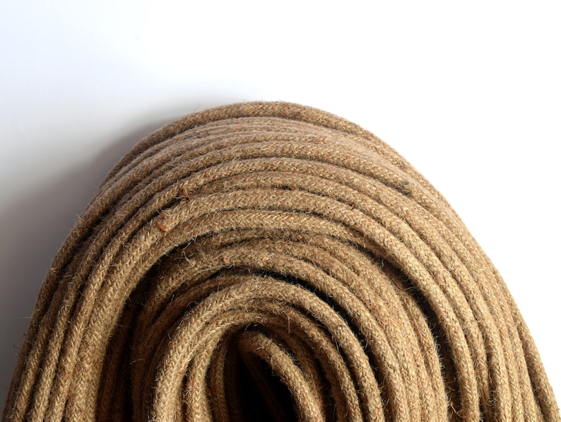 May include: A close-up of a tightly wound coil of natural brown jute rope. The rope is made of thick, twisted fibers and has a rough, textured surface.