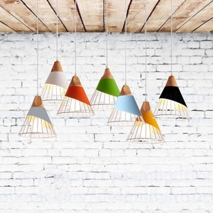Pu&ograve; includere: Una collezione di sette lampade a sospensione appese a cavi bianchi. Ogni lampada presenta una sezione superiore conica in legno collegata a un paralume di colore solido e a una struttura inferiore in filo metallico. I colori includono grigio, bianco, arancione, verde, blu, giallo e nero.
