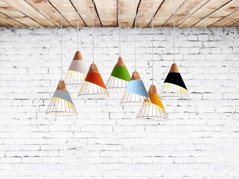 Pu&ograve; includere: Una collezione di sette lampade a sospensione appese a cavi bianchi. Ogni lampada presenta una sezione superiore conica in legno collegata a un paralume di colore solido e a una struttura inferiore in filo metallico. I colori includono grigio, bianco, arancione, verde, blu, giallo e nero.