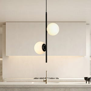 Op de afbeelding: Moderne hanglamp met twee bolvormige, matglazen kappen. De kappen zijn verlicht en hangen aan een zwarte metalen staaf. De lamp is ge&iuml;nstalleerd in een moderne keuken, boven een aanrecht.