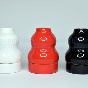May include: Three ceramic vases in different colors: white, red, and black. Each vase has a rounded, bulbous shape with a slightly indented middle section. The vases are all the same size and shape.
