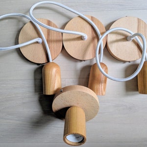 May include: A set of four wooden pendant light fixtures with white cords. Each fixture has a round wooden base and a cylindrical wooden shade.