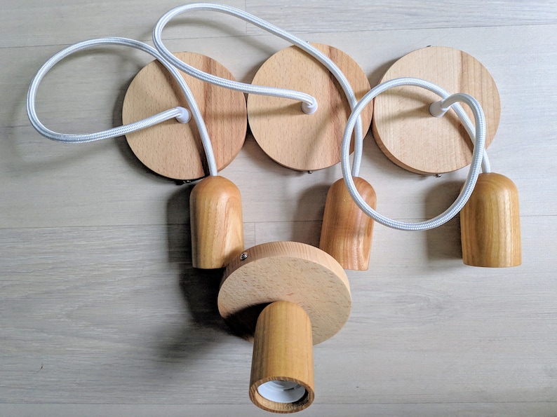May include: A set of four wooden pendant light fixtures with white cords. Each fixture has a round wooden base and a cylindrical wooden shade.