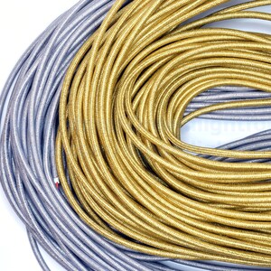 May include: A close-up of two spools of cord, one silver and one gold. The cords are wound tightly together, creating a swirling pattern.