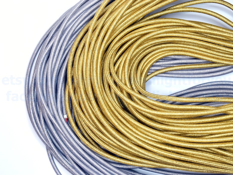 May include: A close-up of two spools of cord, one silver and one gold. The cords are wound tightly together, creating a swirling pattern.