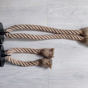 May include: Two pendant light fittings featuring black circular ceiling mounts with exposed electrical wires. Each fitting consists of a thick, natural-coloured jute rope looped through the mount, ending in two frayed, knotted rope ends.