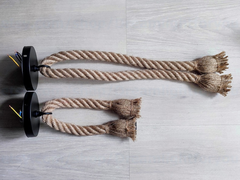 May include: Two pendant light fittings featuring black circular ceiling mounts with exposed electrical wires. Each fitting consists of a thick, natural-coloured jute rope looped through the mount, ending in two frayed, knotted rope ends.