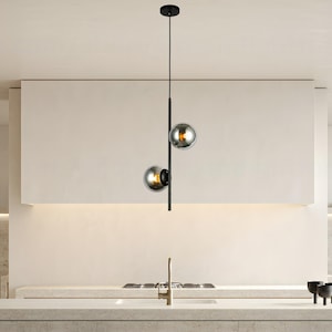 Op de afbeelding: Moderne hanglamp met twee bolvormige rookglazen kappen. De lamp hangt aan een zwart metalen frame aan het plafond. Deze stijlvolle lamp voegt een moderne touch toe aan een keuken.
