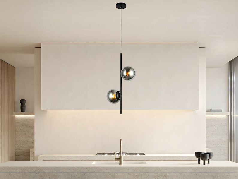 Op de afbeelding: Moderne hanglamp met twee bolvormige rookglazen kappen. De lamp hangt aan een zwart metalen frame aan het plafond. Deze stijlvolle lamp voegt een moderne touch toe aan een keuken.