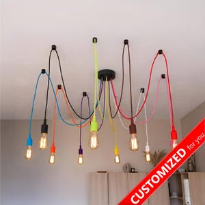May include: A multi-light pendant chandelier featuring ten individual bulbs suspended from a central black ceiling mount by colorful fabric cords in blue, black, orange, purple, lime green, yellow, brown, white, pink, and red.