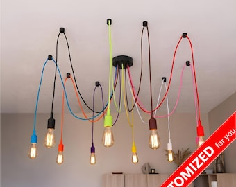 Puede incluir: Una lámpara de techo con múltiples luces que cuenta con diez bombillas individuales suspendidas de un soporte central negro mediante cables de tela de colores en azul, negro, naranja, morado, verde lima, amarillo, marrón, blanco, rosa y rojo.