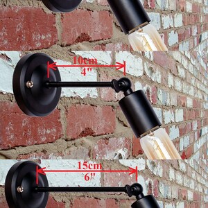K&ouml;nnte beinhalten: Drei schwarze Wandleuchten mit verstellbaren Armen. Die Arme sind 5 cm, 10 cm und 15 cm lang. Die Leuchten sind vor einer Backsteinwand abgebildet.
