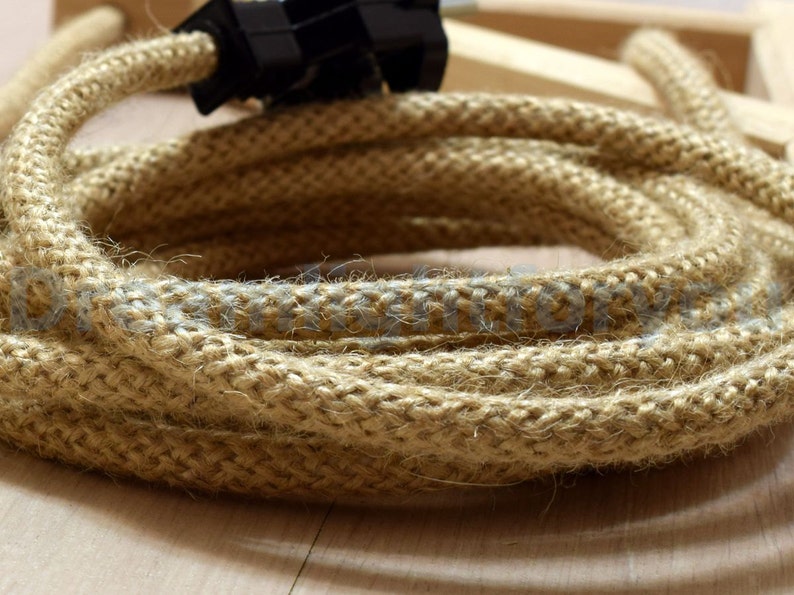 May include: Close-up of a thick, natural-fiber cord with a light brown color and a subtle gray stripe running along the length. The cord is woven with a textured, rope-like pattern.