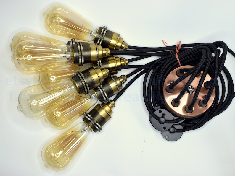 May include: A six-light pendant light kit with black braided cord and copper ceiling plate. The kit includes six clear glass bulbs with gold-tone metal sockets.